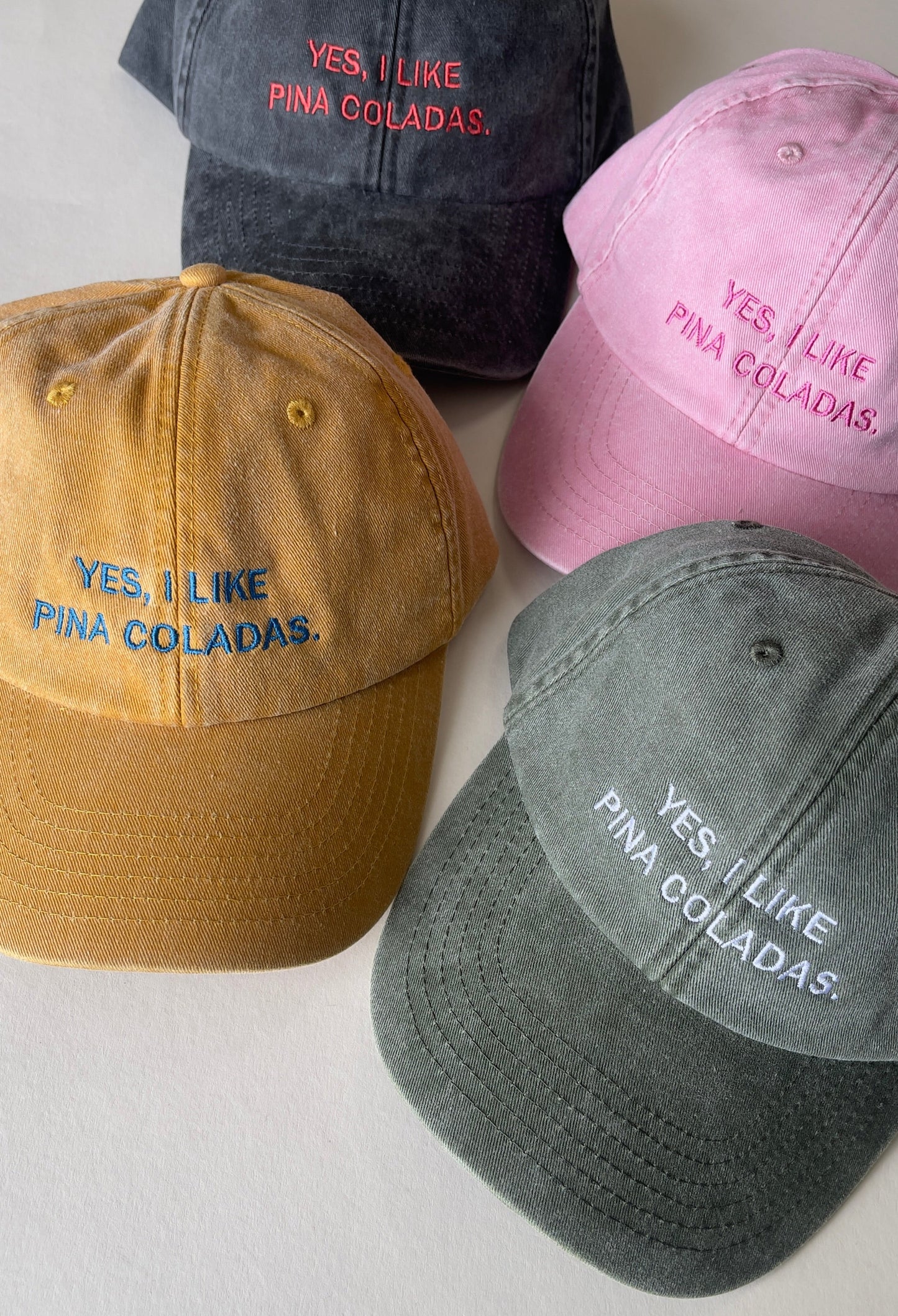 Four colorful baseball caps with 'YES, I LIKE PINA COLADAS' text on a light gray background.