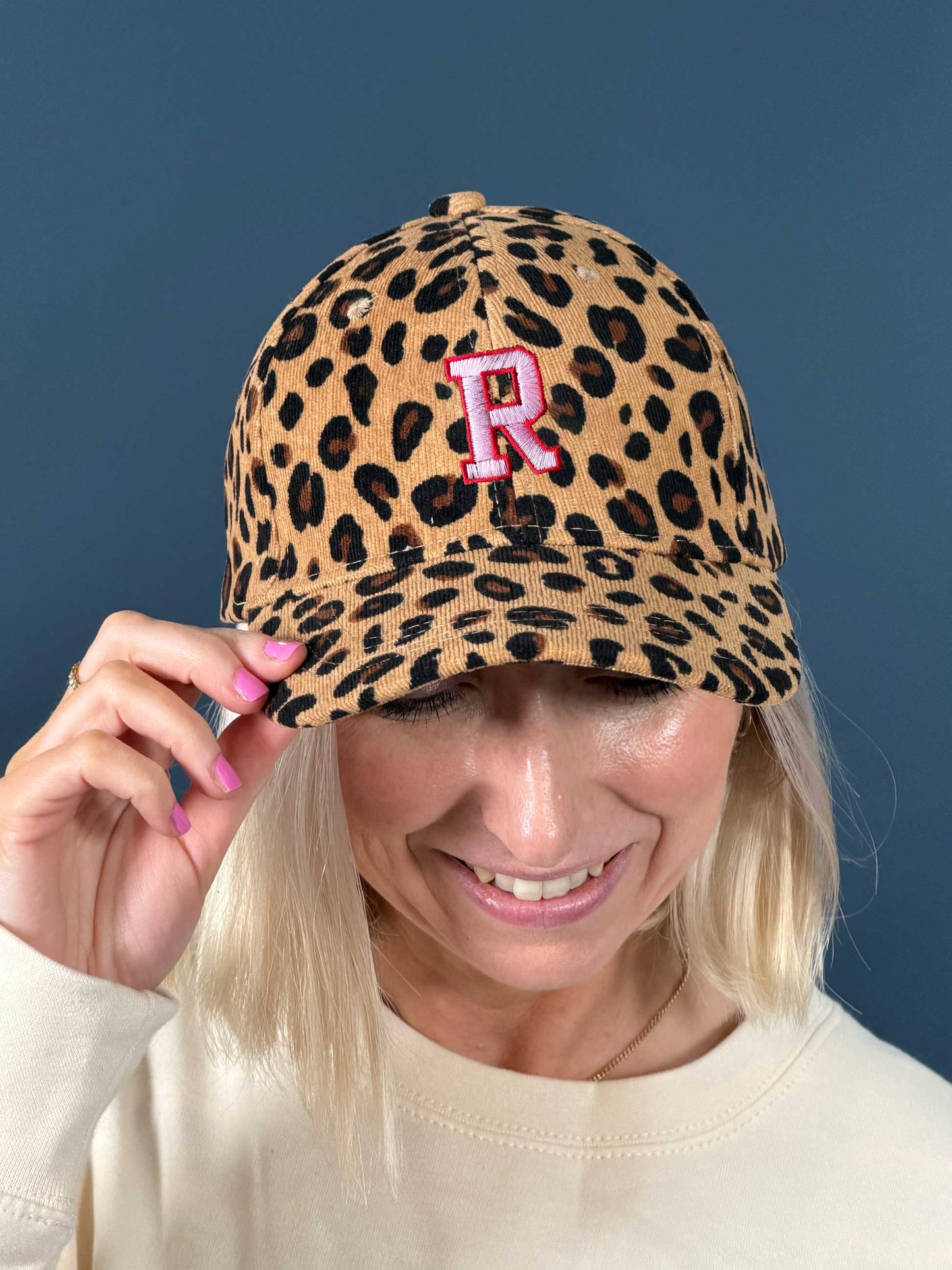 Person wearing a leopard print cap with a pink and red embroidered 'R'