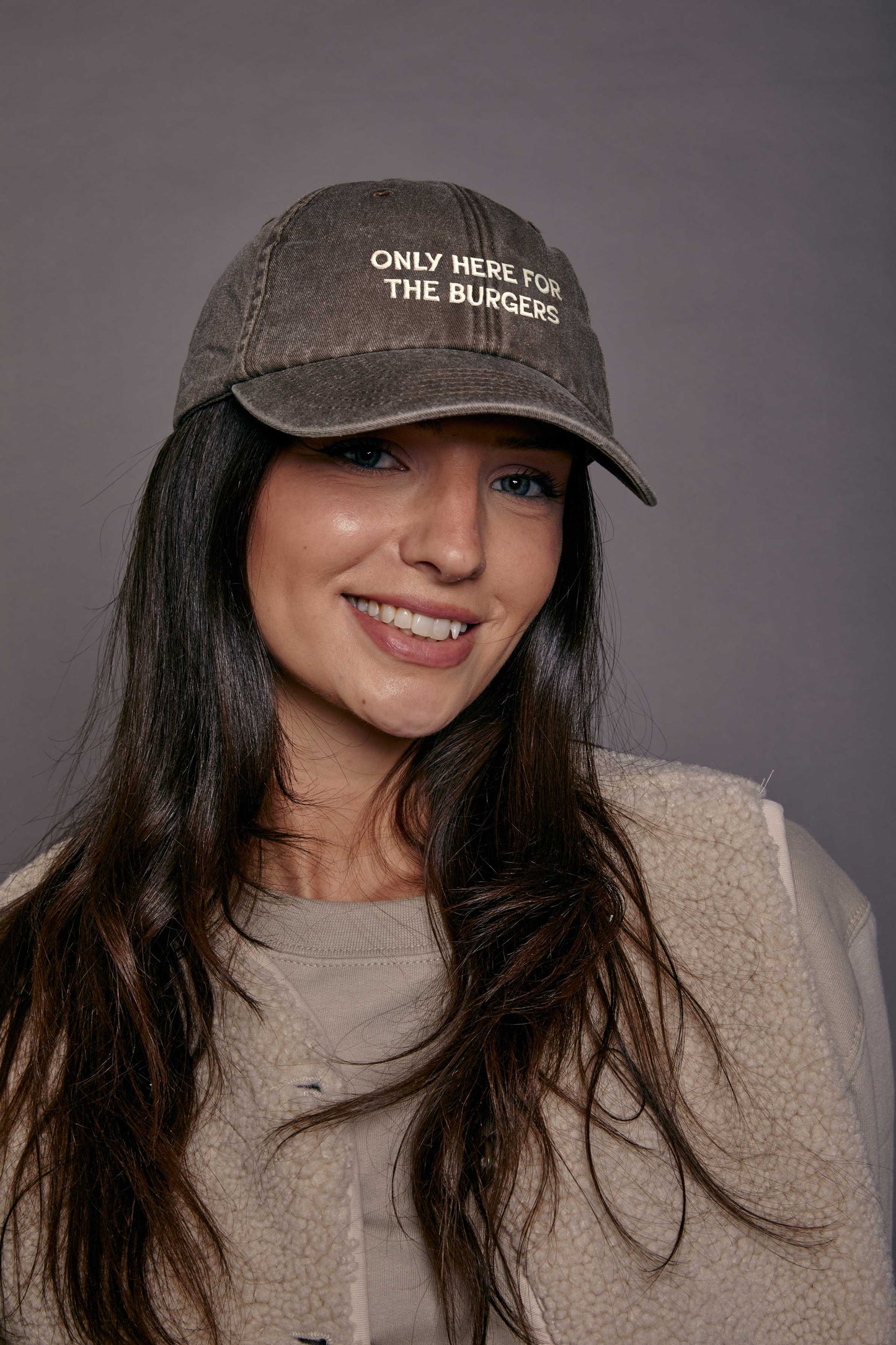 Woman wearing a cap with text 'only here for the burgers' on a grey background