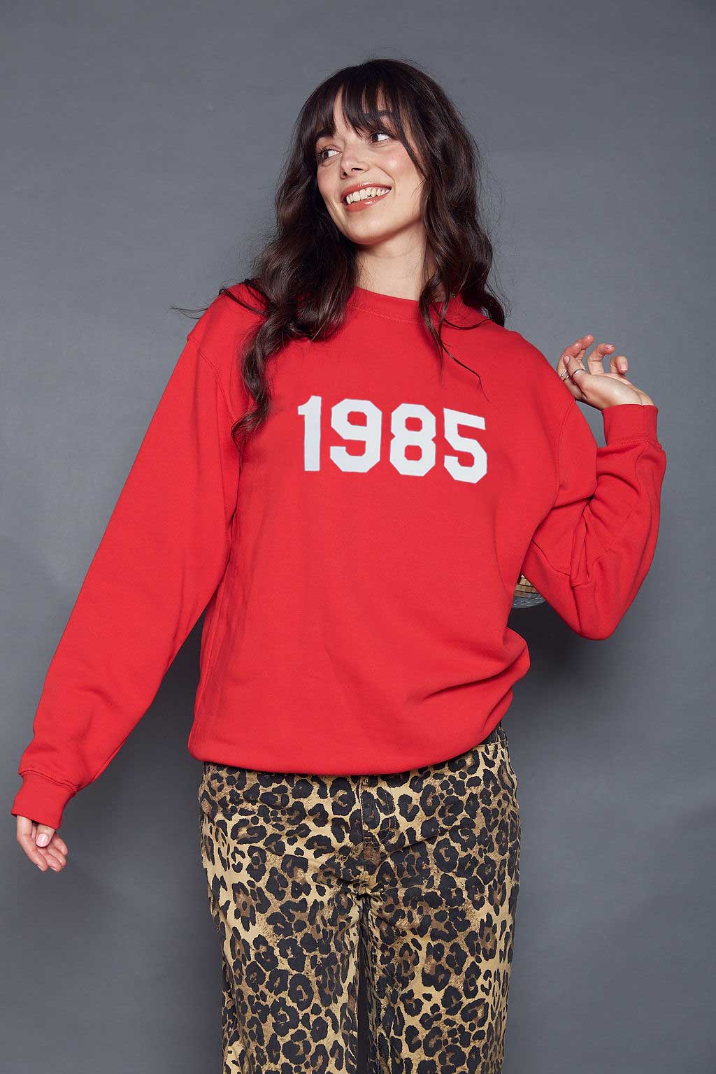 A woman wearing a bright red pullover sweatshirt printed with the year '1985' in white text on the front