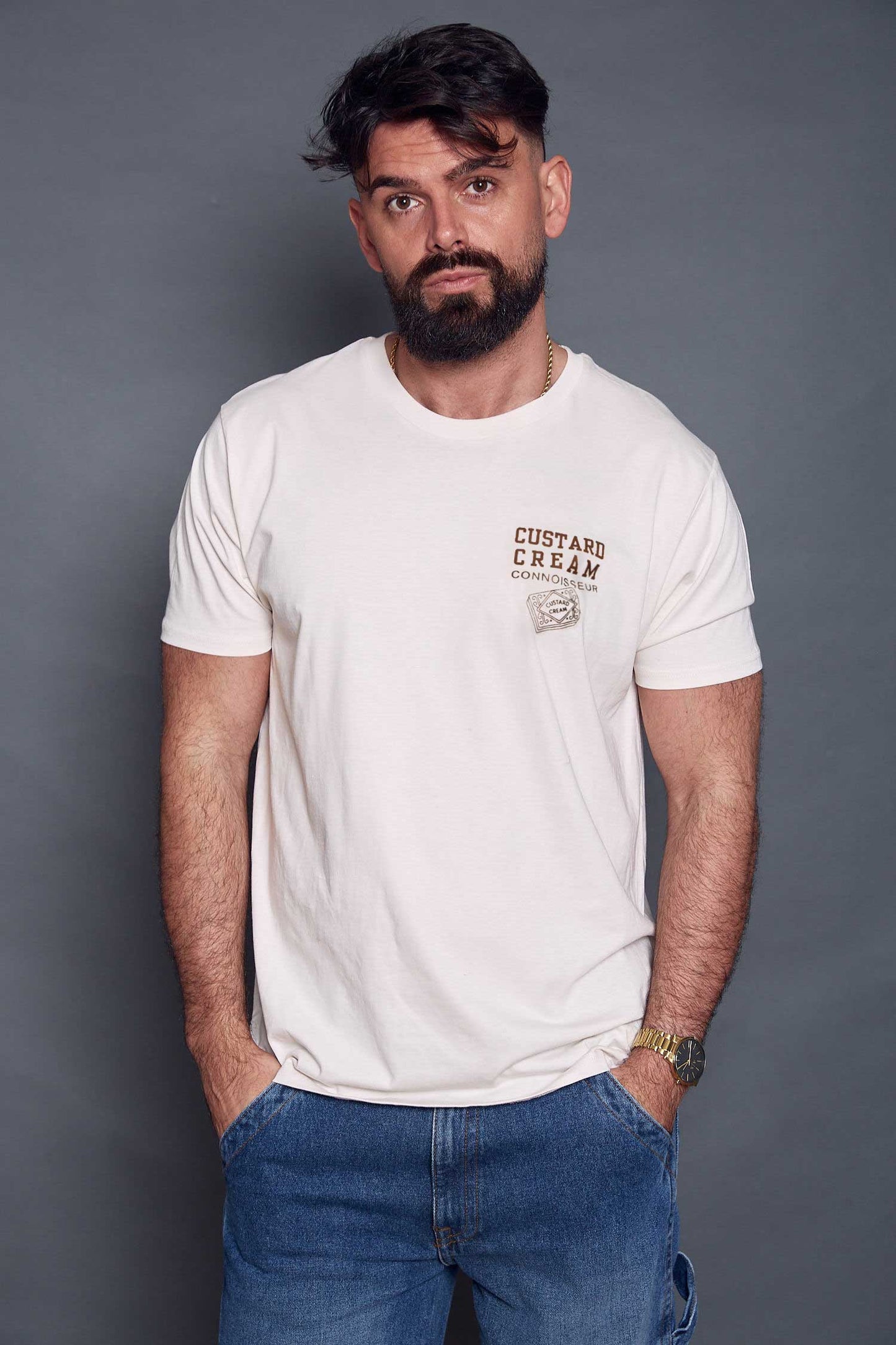 Man wearing a cream t-shirt with custard cream text and blue jeans against a grey background