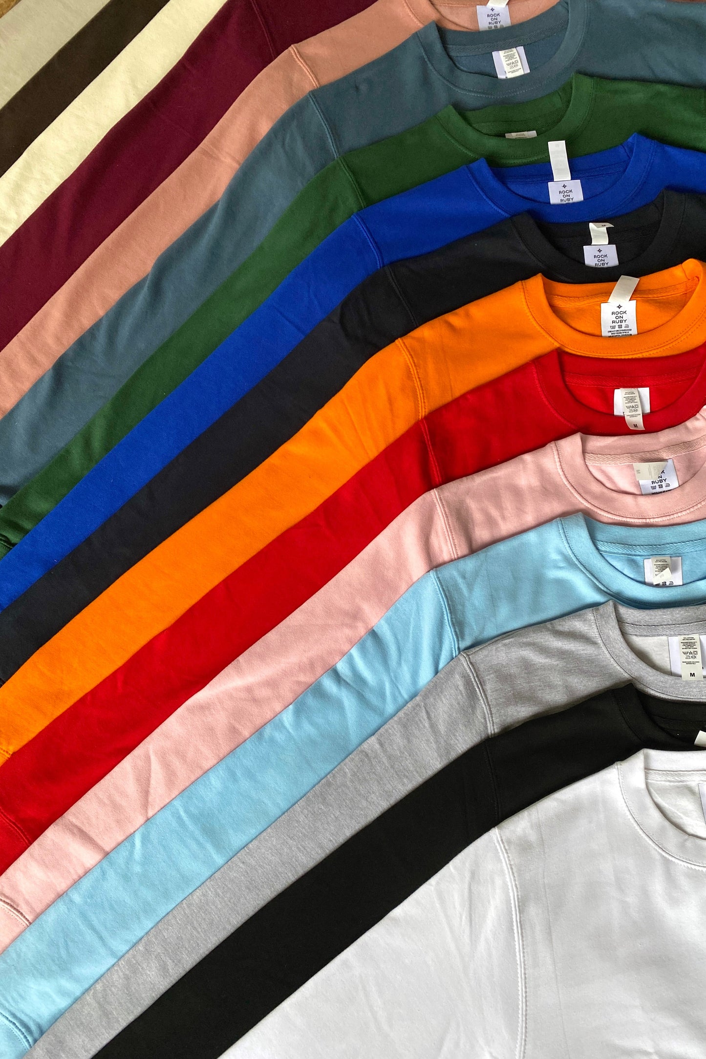 Row of colorful sweatshirts with Rock On Ruby tags on a wood background