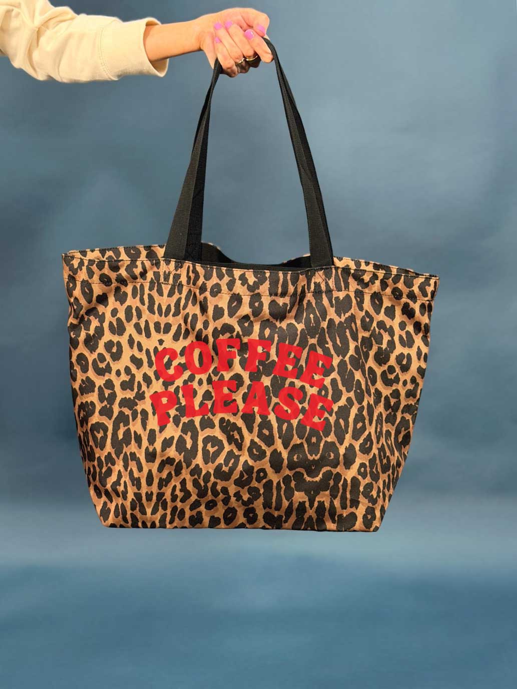 Leopard print tote bag with 'Coffee Please' text in red held by a person against a blue background
