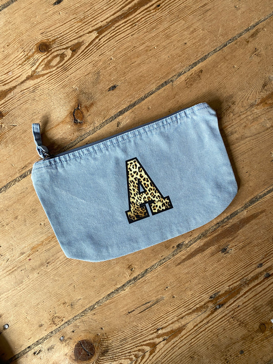 Light blue pouch bag with a leopard print letter 'A' on a wooden surface