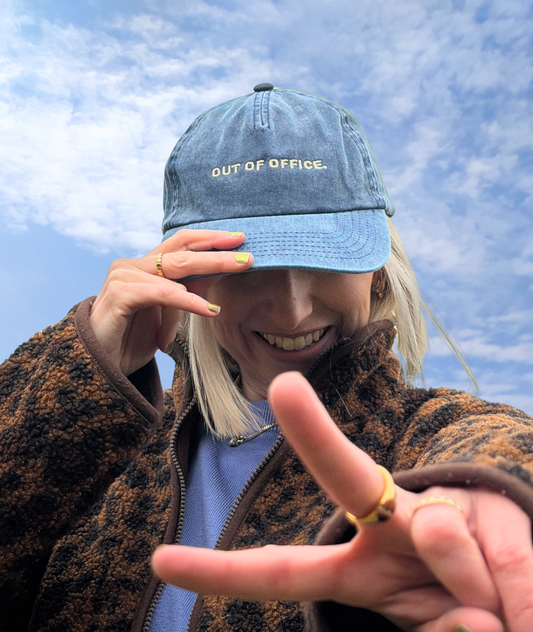 Person wearing a blue cap with 'OUT OF OFFICE.' text against a blue sky.
