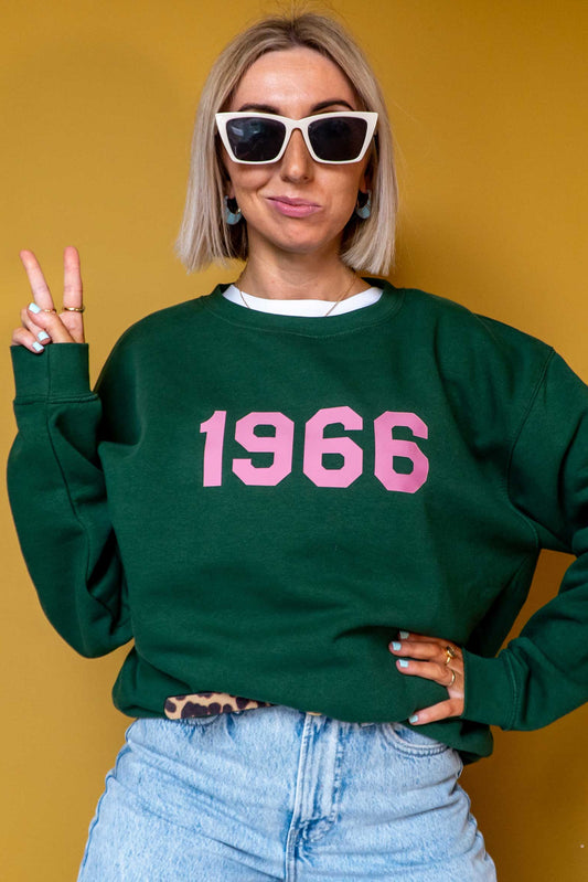 Woman wearing a green sweatshirt with '1966' in pink on a mustard yellow background