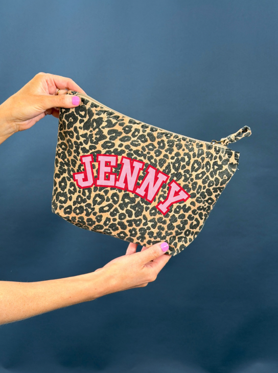 Leopard print bag with 'JENNY' text in pink held by a person against a blue background