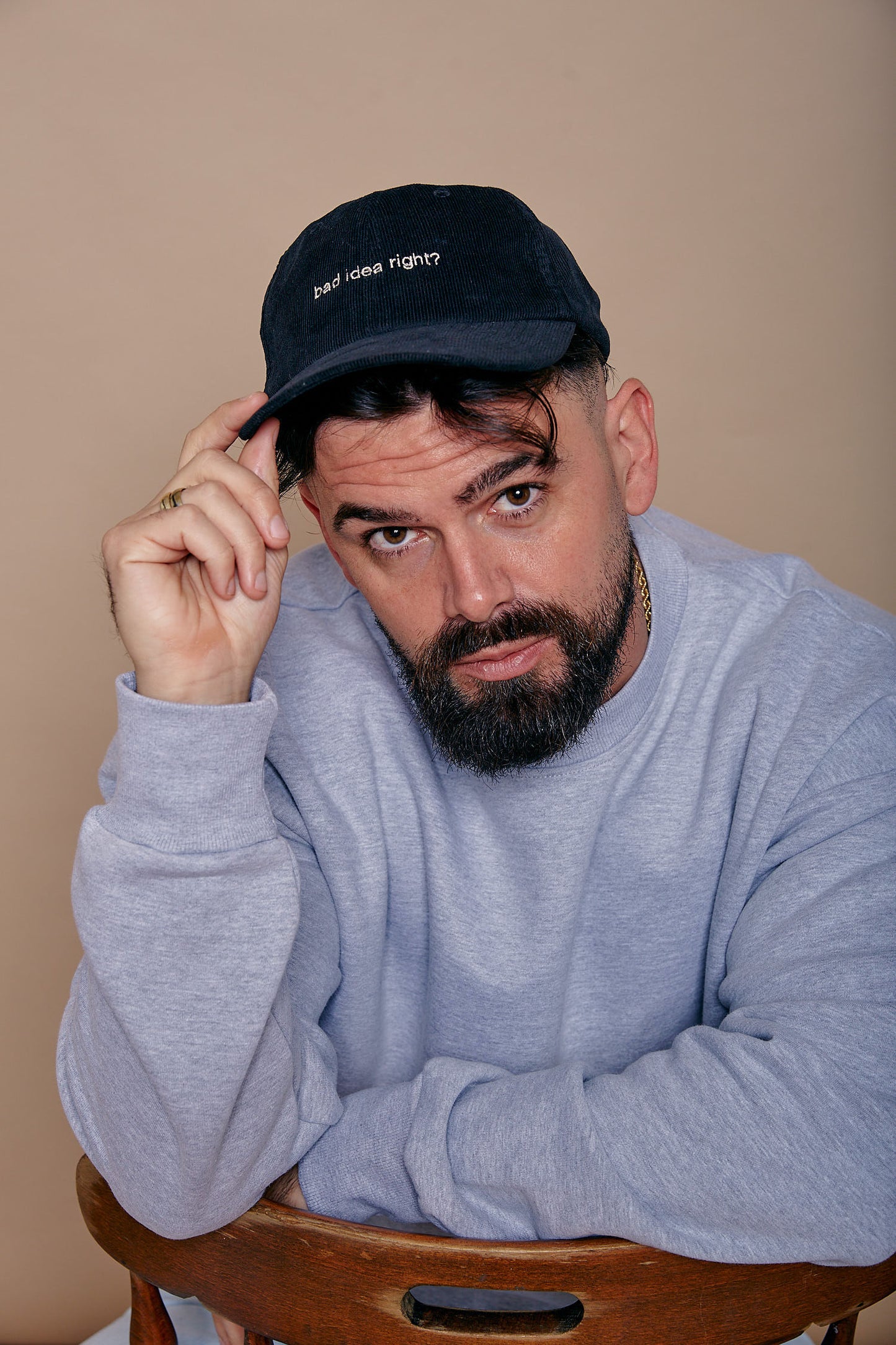 man wearing black cord cap embroidered with the slogan 'bad idea right?' in white thread