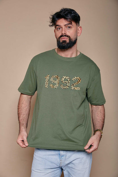 Man wearing a green t-shirt with '1992' printed on it in leopard print stood against a beige background