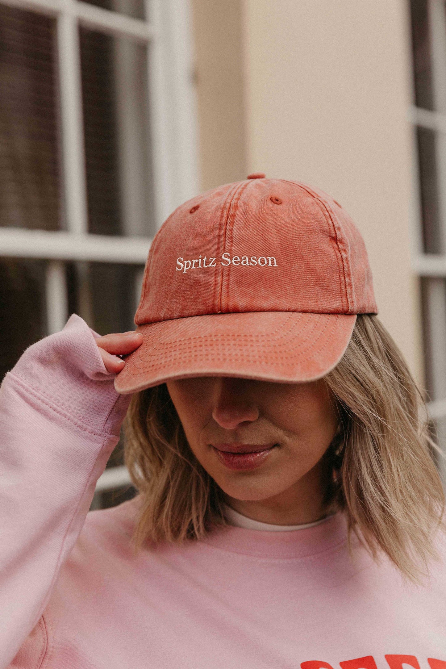 A person wearing a faded orange baseball cap with the slogan 'Spritz Season' embroidered on the front.