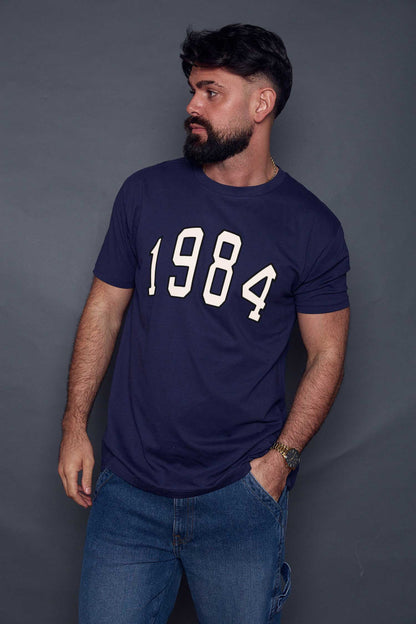 Man wearing a navy blue t-shirt with '1984' printed on it against a grey background
