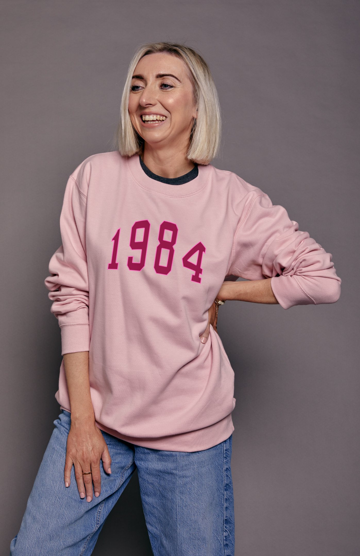 Person wearing a pink sweatshirt with '1984' printed on it against a grey background