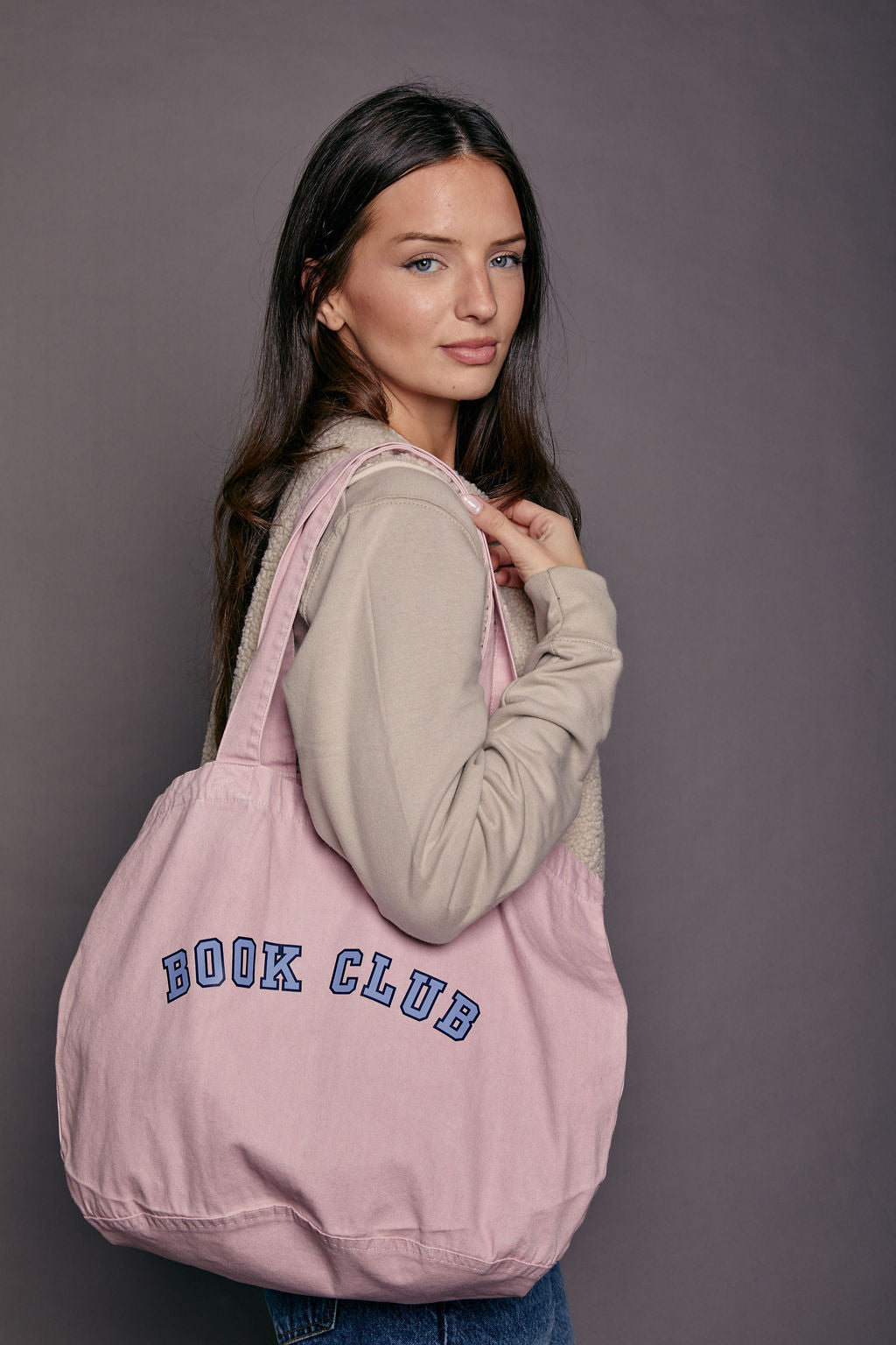 Woman holding a pink tote bag with 'BOOK CLUB' text against a gray background