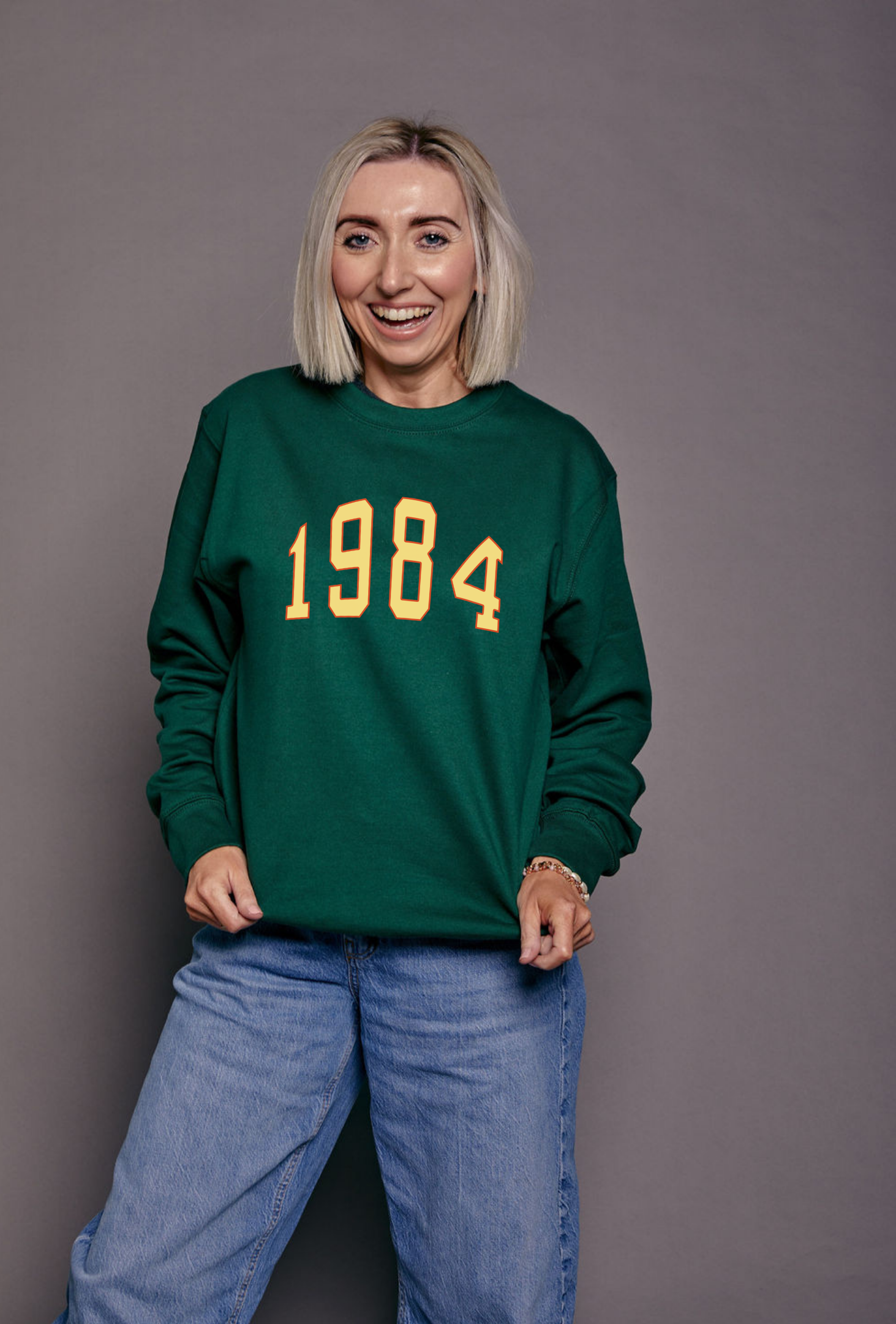 Person wearing a green sweatshirt with '1984' printed on it against a gray background