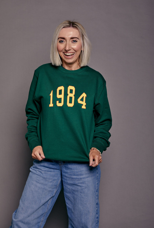 Person wearing a green sweatshirt with '1984' printed on it against a gray background