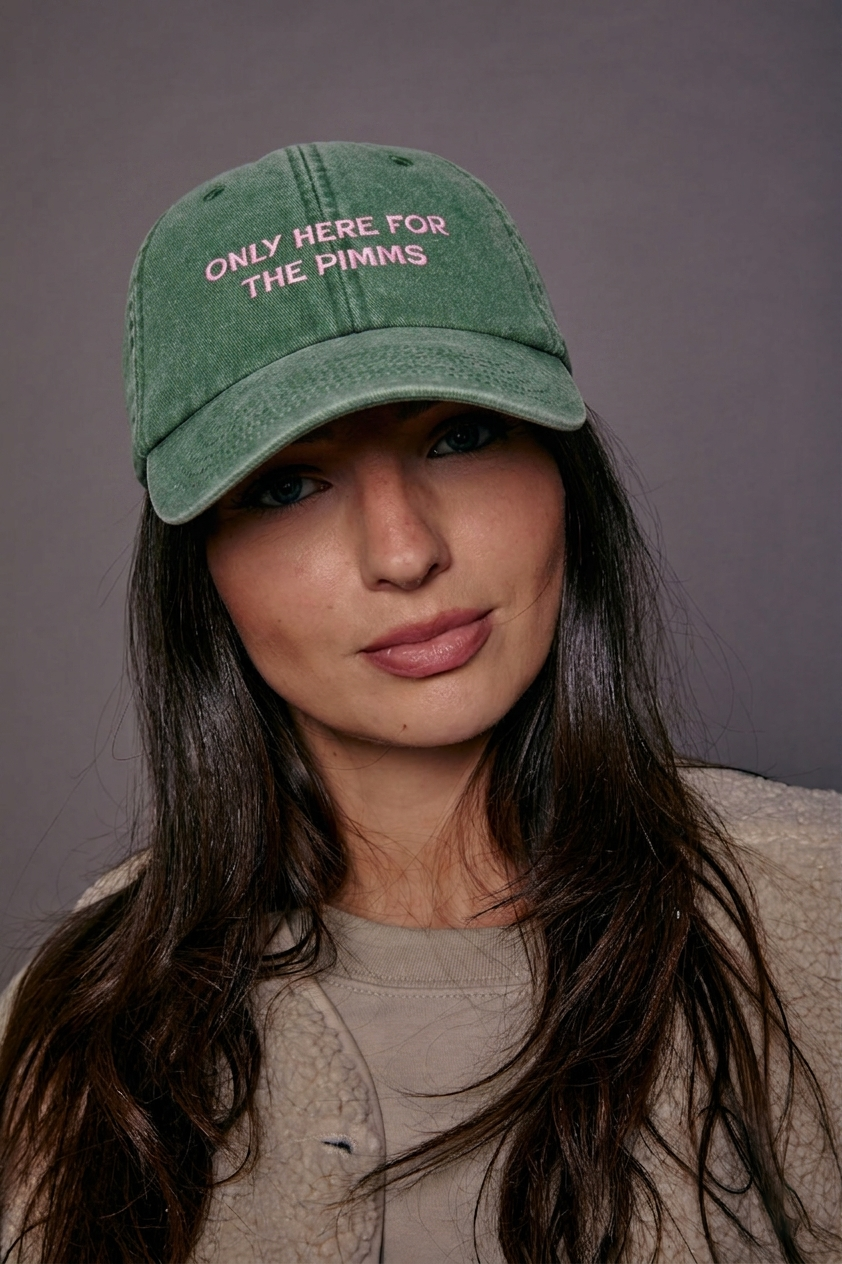 Person wearing a green cap with text 'only here for the pimms' against a grey background