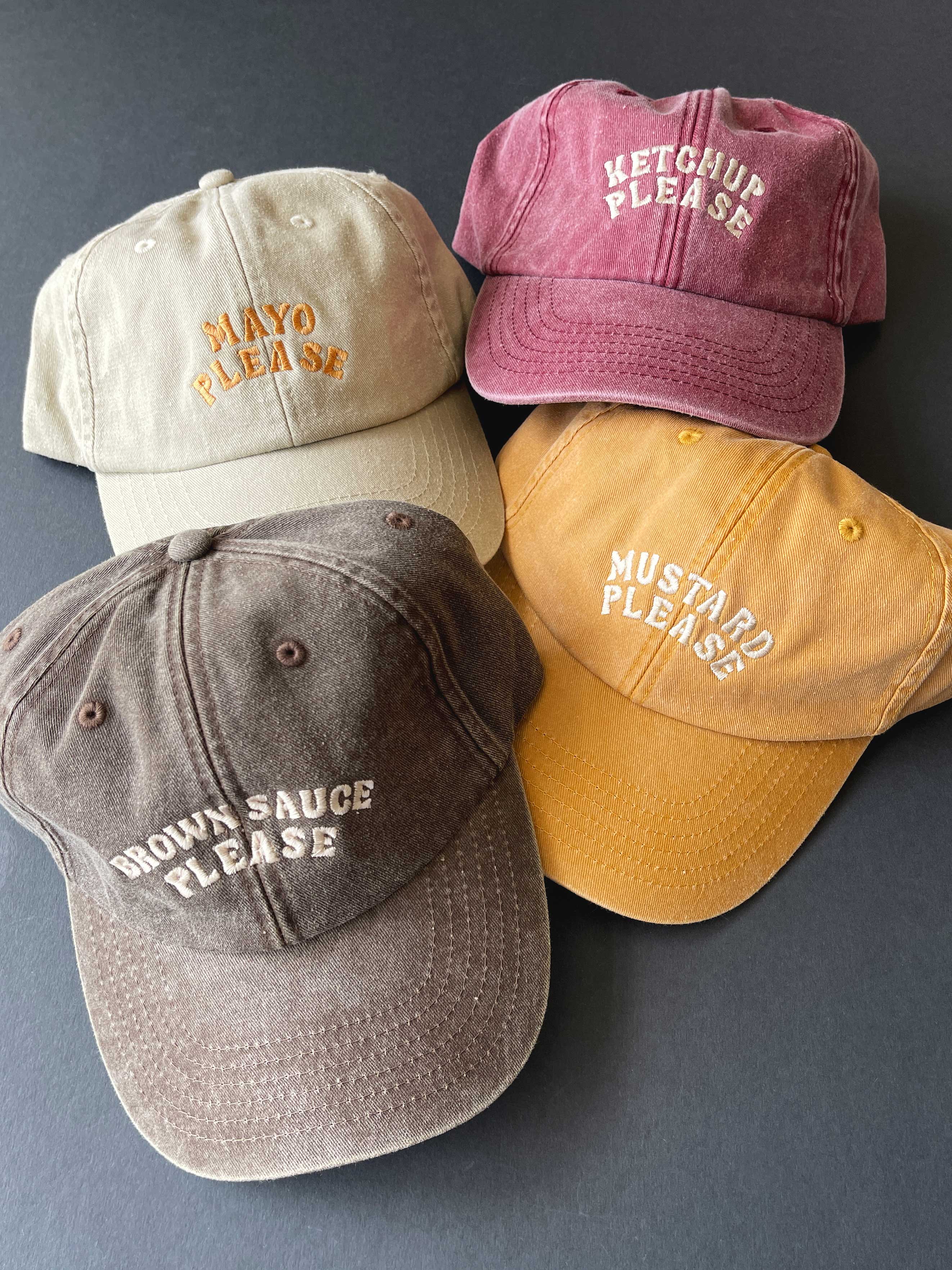 Four baseball caps with humorous condiment-themed text on a grey background