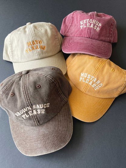 Four baseball caps with humorous condiment-themed text on a grey background