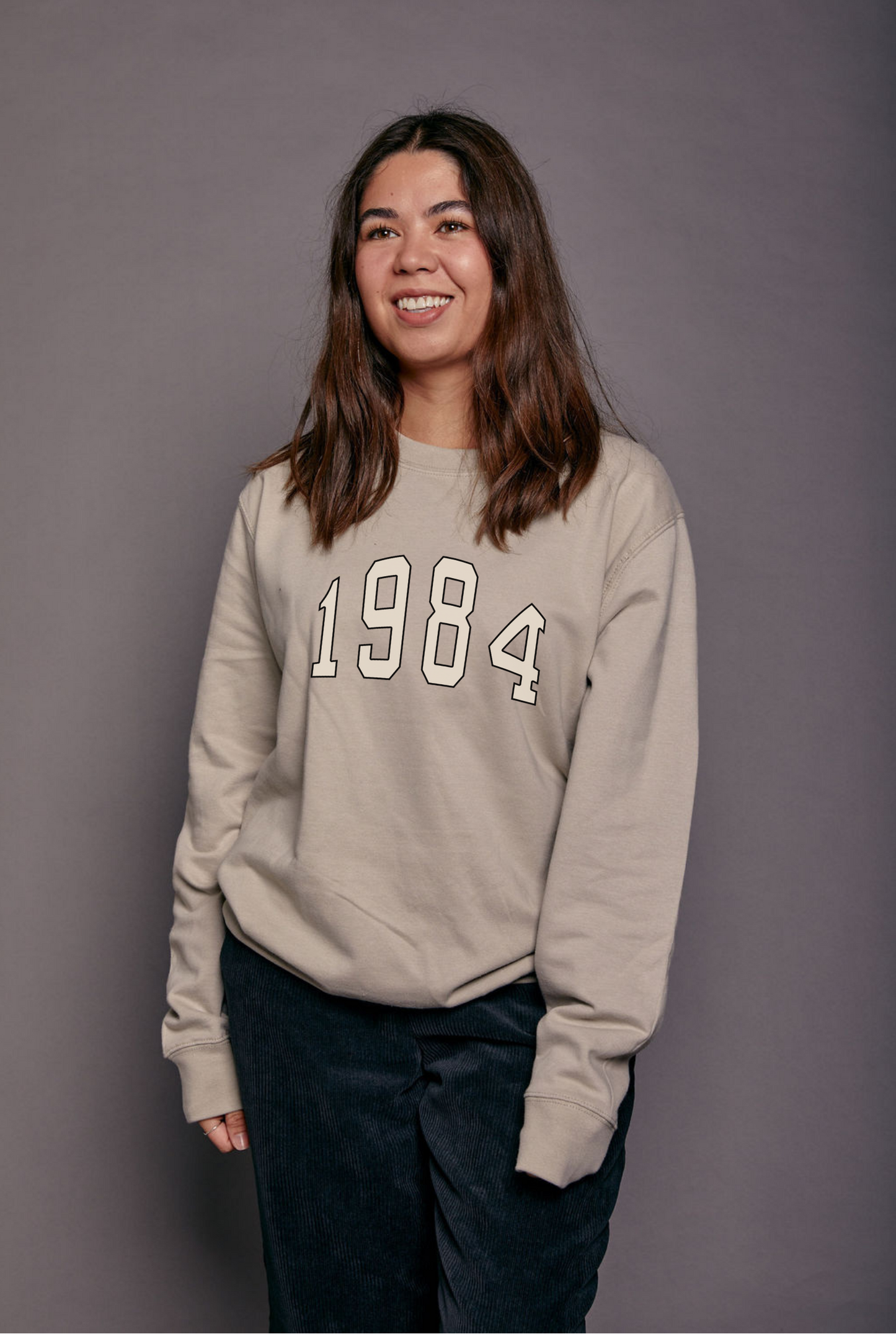 Person wearing a cream/grey sweatshirt with '1984' printed on it against a plain background