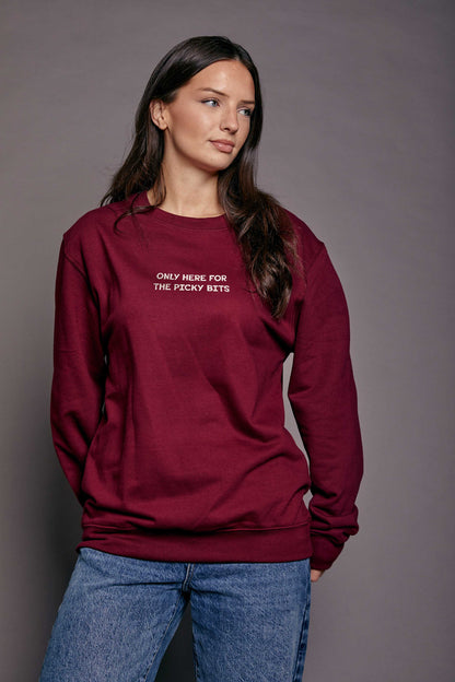 Woman wearing a maroon sweatshirt with text 'only here for the picky bits' against a grey background