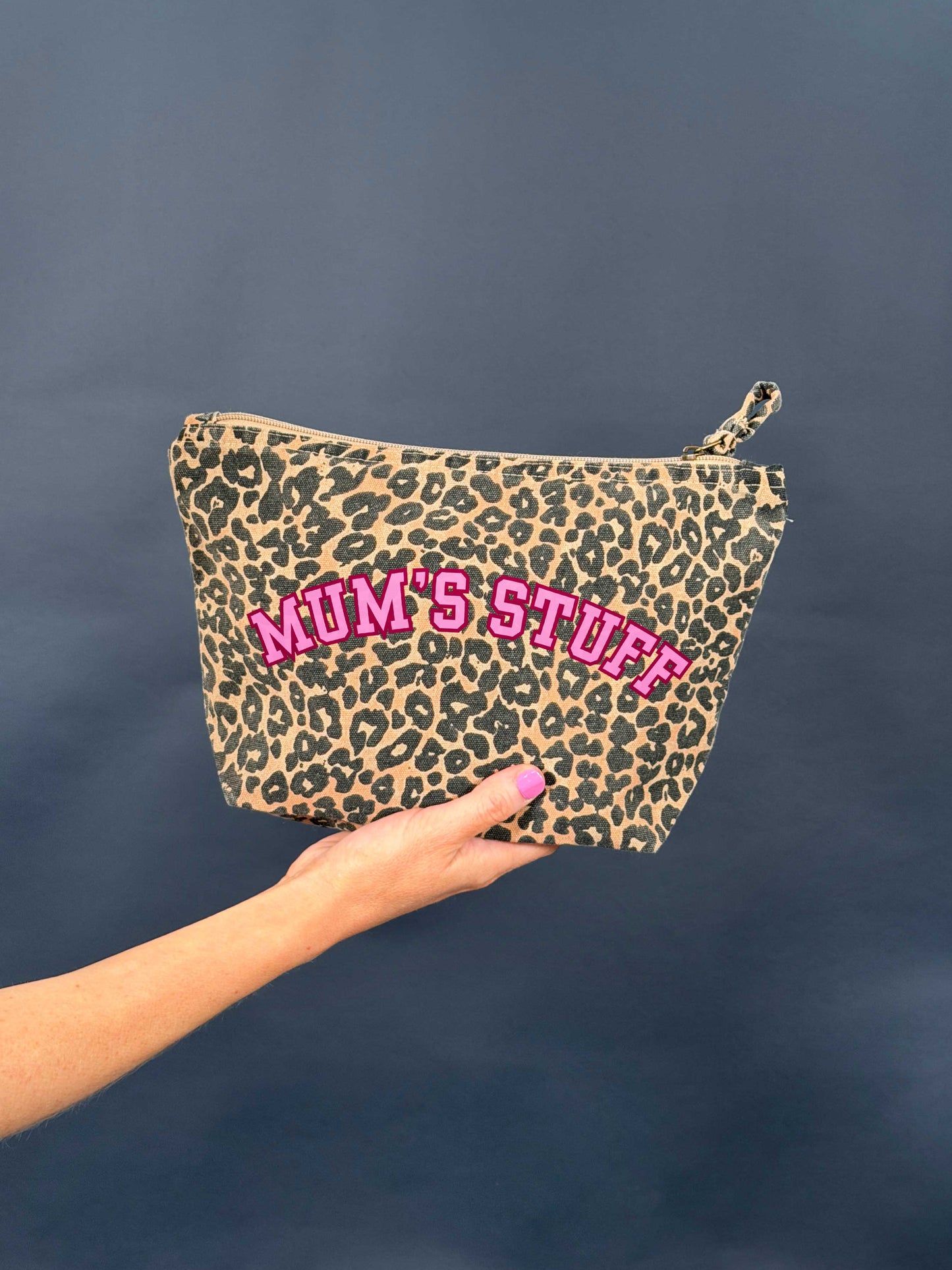 Leopard print pouch with 'MUM'S STUFF' text in pink held by a hand against a dark background