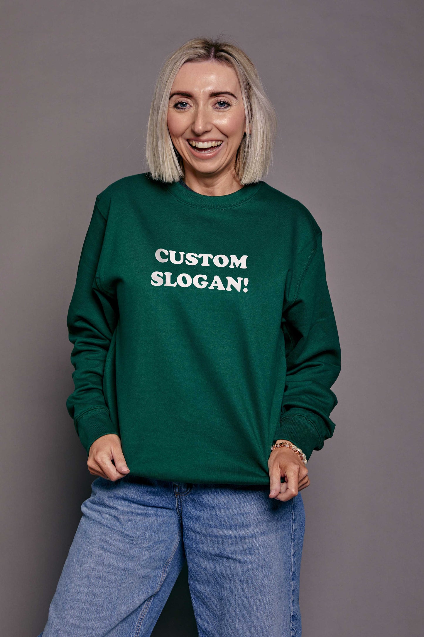 Person wearing a bottle green sweatshirt with 'CUSTOM SLOGAN!' text printed in white across the front