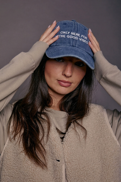 Person wearing a blue denim cap with text 'only here for the good vibes', against a plain background