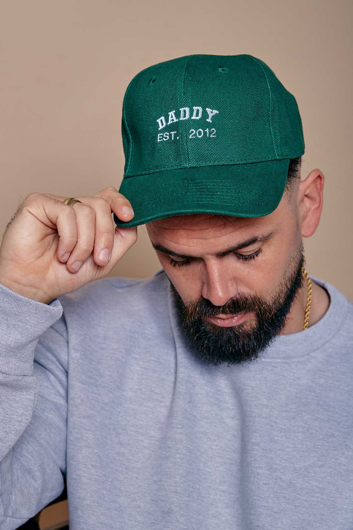 Man wearing a green cap with 'Daddy Est. 2012' text against a beige background