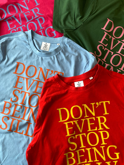 Three graphic t-shirts in red, light blue, hot pink and dark green, arranged diagonally. Each shirt features the text 'DON'T EVER STOP BEING SILLY' in a large, bold, serif font in contrasting colors (orange, yellow, and pink respectively).