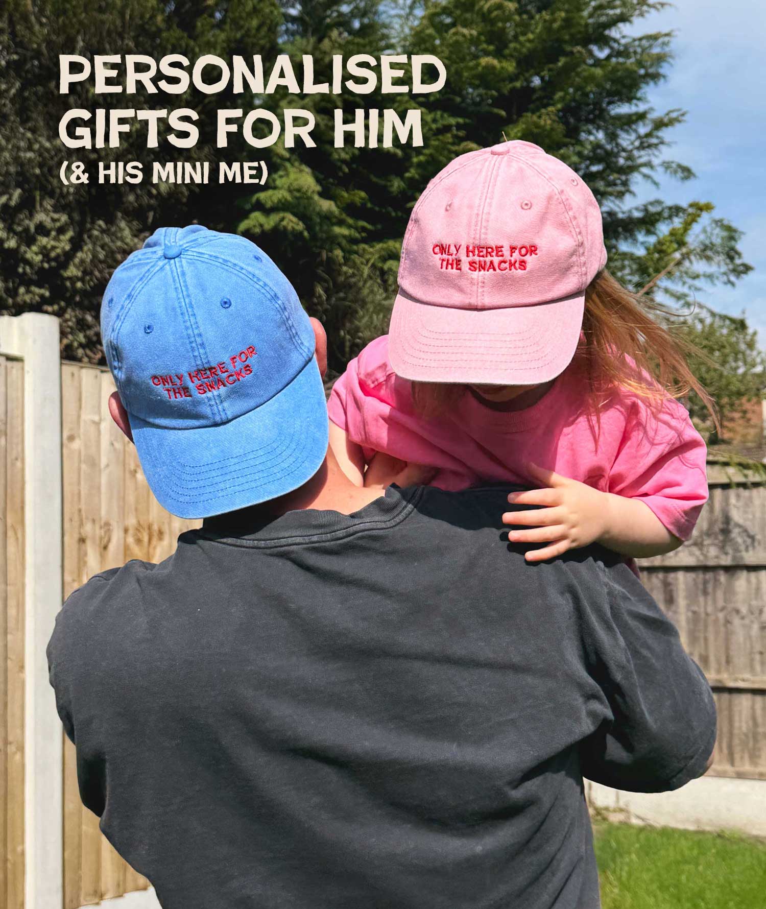 Person holding a child wearing pink and blue caps with personalised text outdoors.