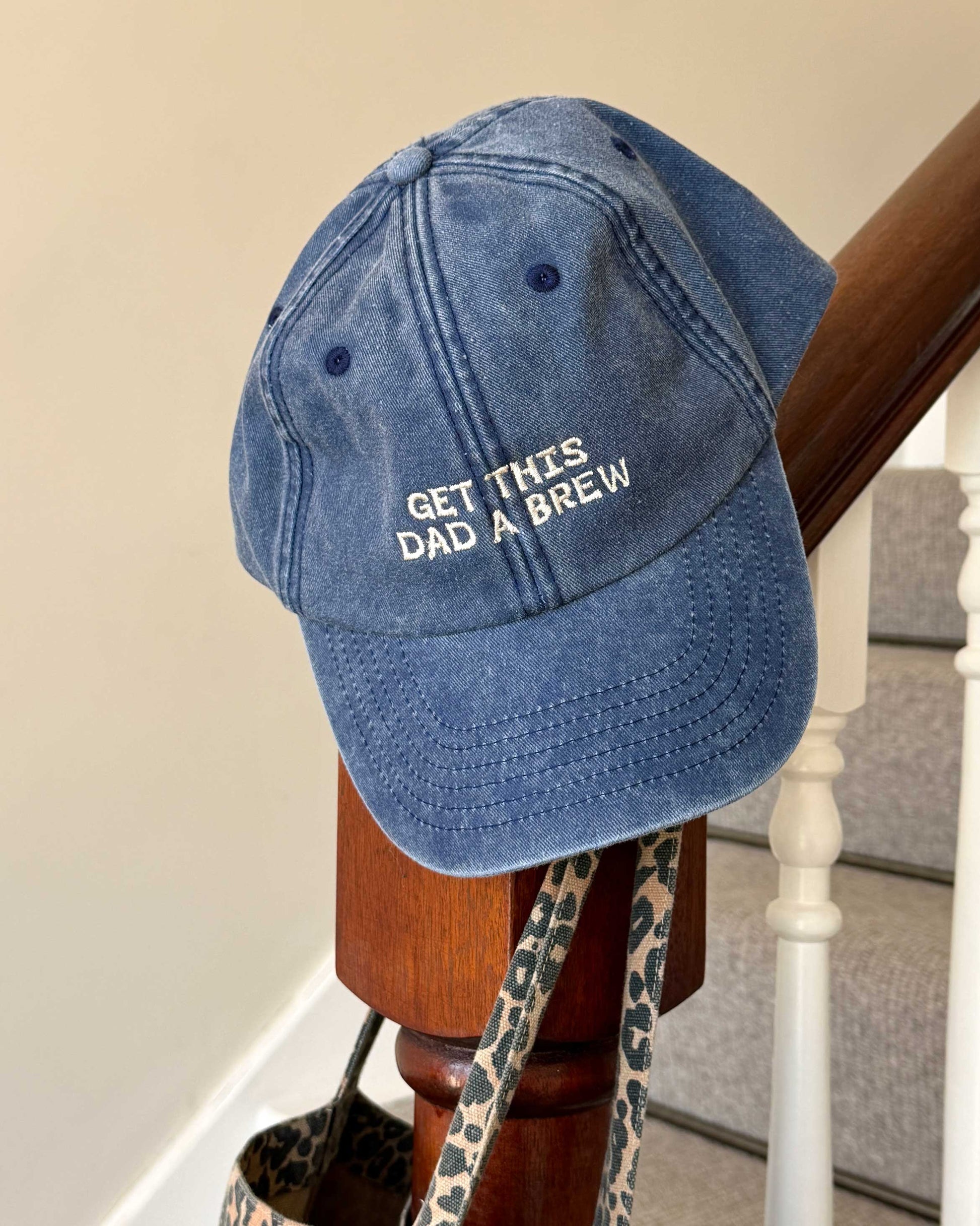 Blue cap with 'Get this dad a brew' text on a wooden stand.
