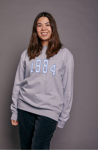 Person wearing a grey sweatshirt with '1984' printed on it against a grey background