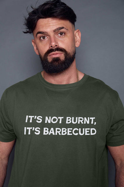 Man wearing a khaki green t-shirt with text 'IT'S NOT BURNT, IT'S BARBECUED' against a grey background