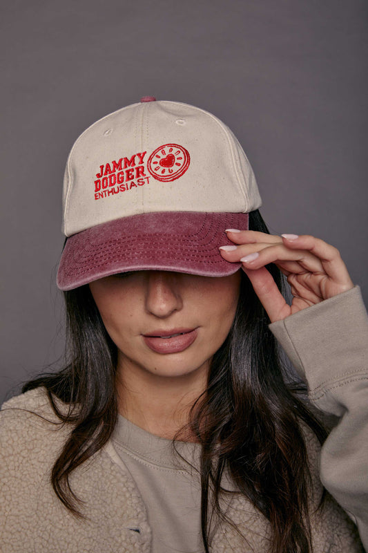woman wearing a two tone faded cap in cream and red embroidered on the front with the slogan 'jammy dodger enthusiast'