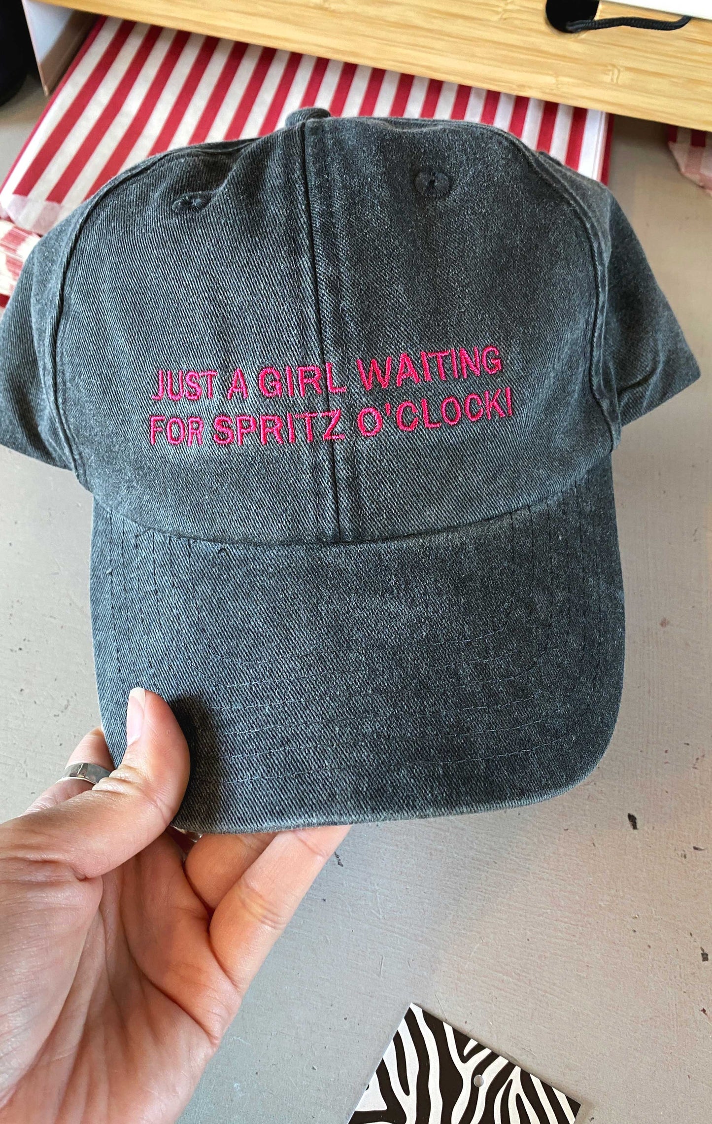 vintage black cap with pink 'spritz o'clock' text held by a hand on a neutral background