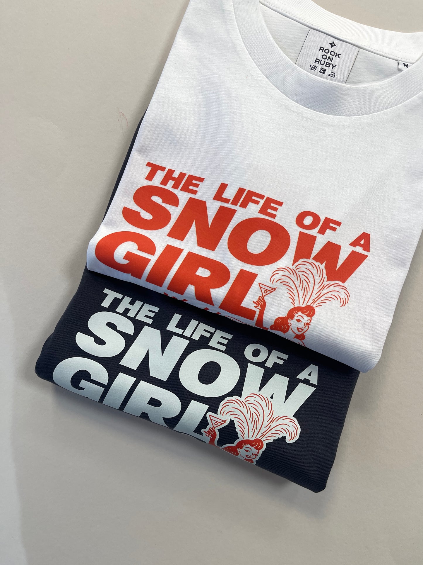 Two folded t-shirts with 'The Life of Snow Girl' design on a neutral background