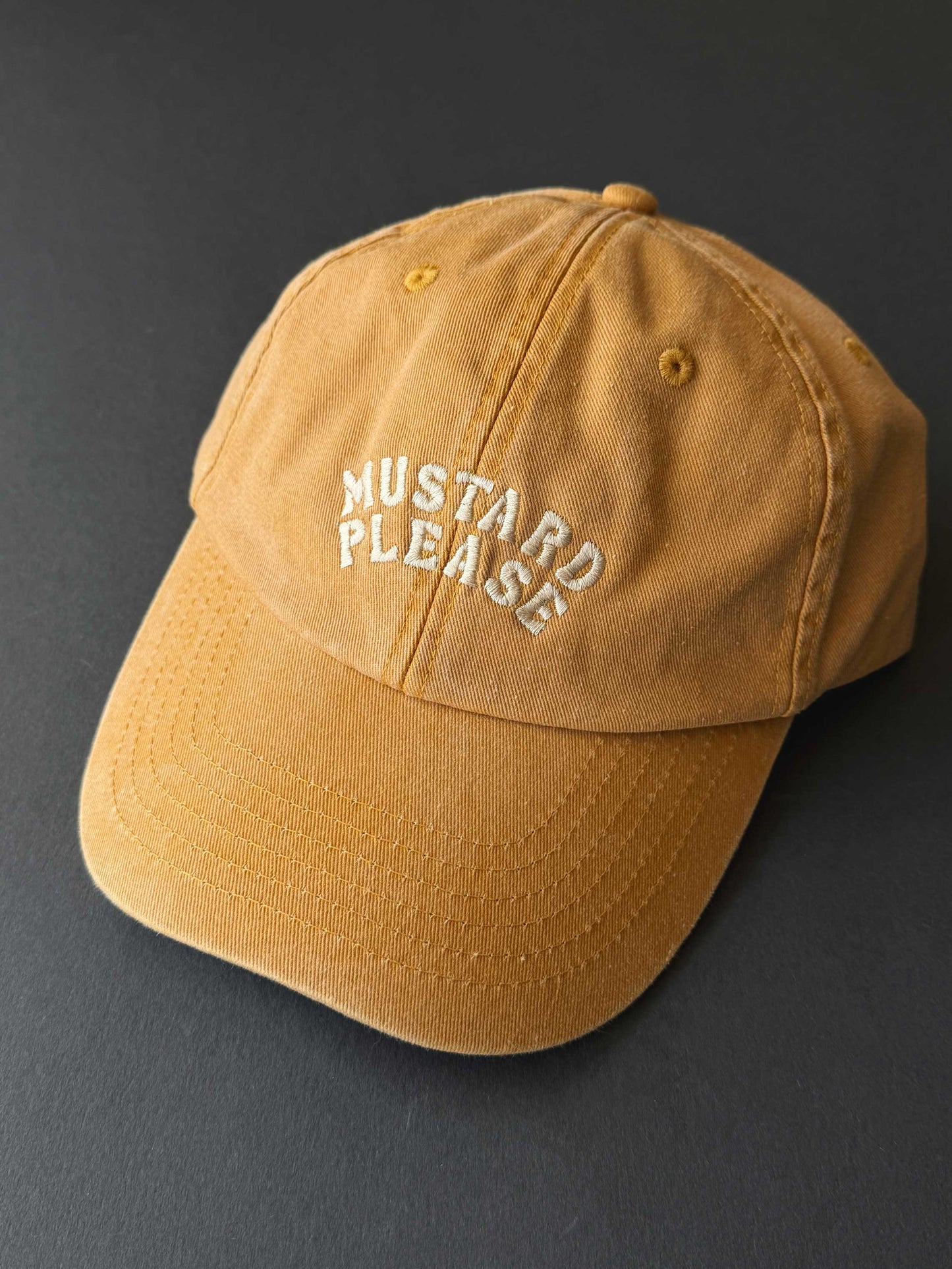 faded yellow cap with 'Mustard Please' text on a dark background