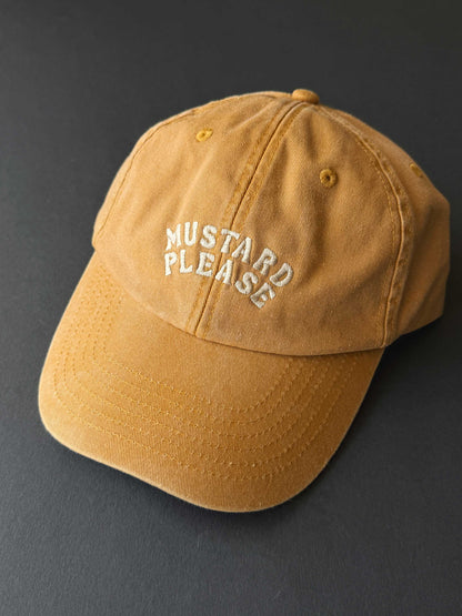 faded yellow cap with 'Mustard Please' text on a dark background