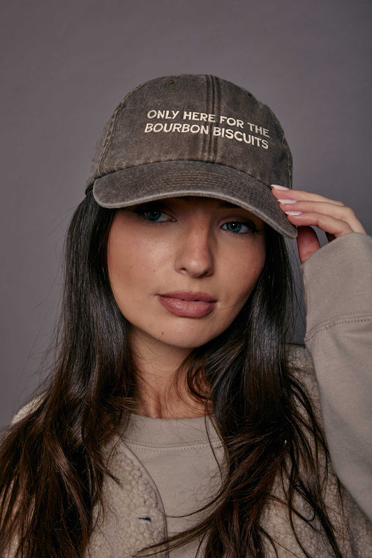 Woman wearing a cap with text 'only here for the bourbon biscuits', against a grey background