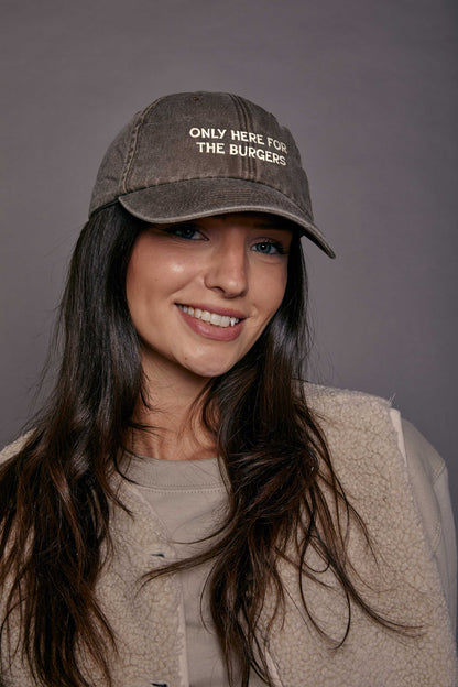 Woman wearing a cap with text 'only here for the burgers' on a grey background
