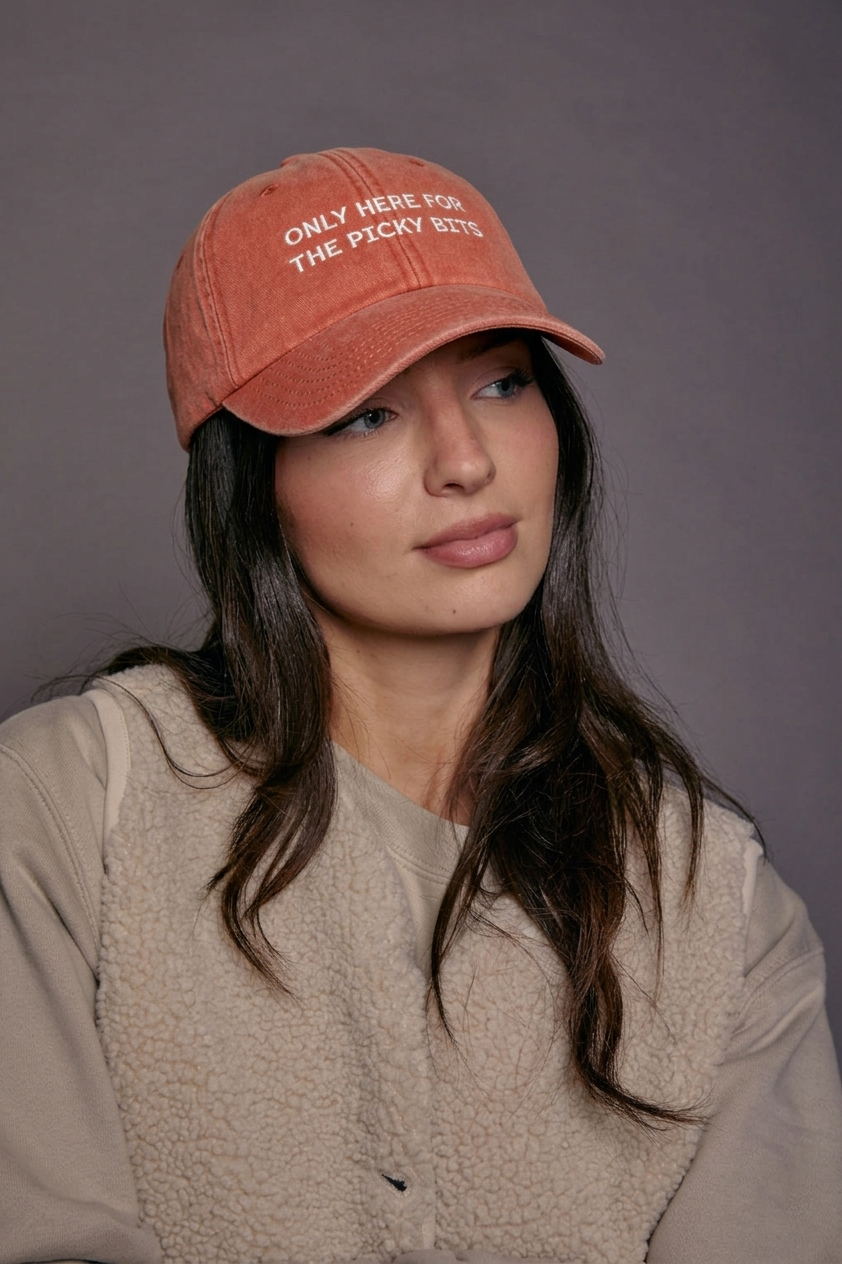 Woman wearing an orange cap with text 'only here for the picky bits' against a grey background