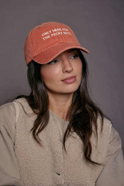 Woman wearing an orange cap with text 'only here for the picky bits' against a grey background