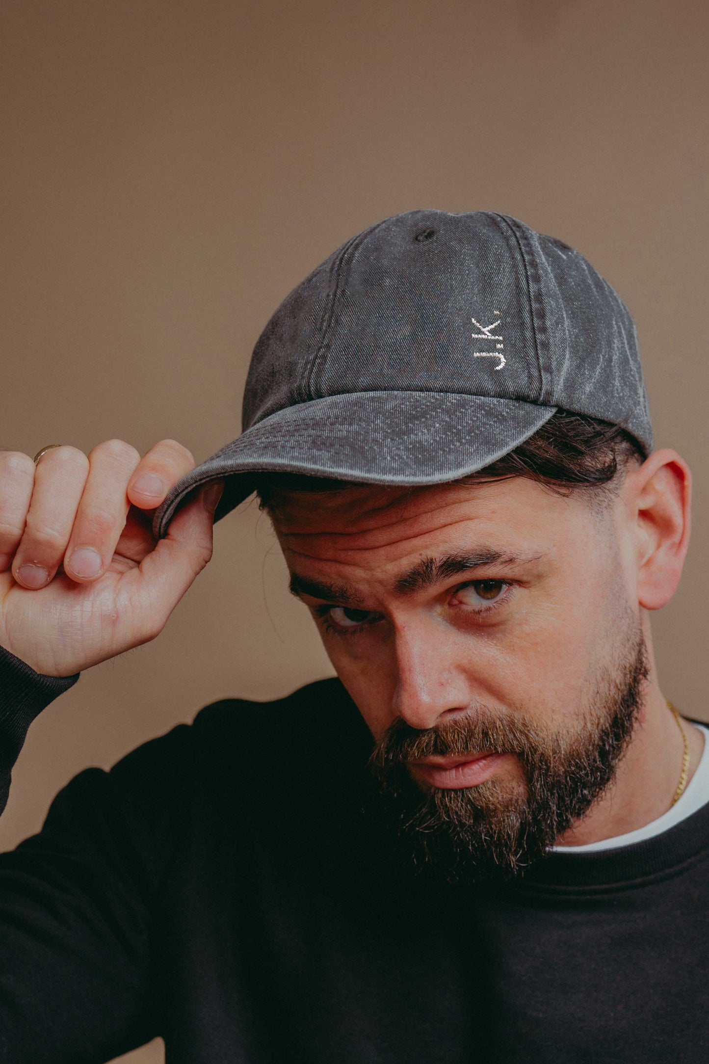 Man wearing a grey cap with 'JK' initials  against a beige background