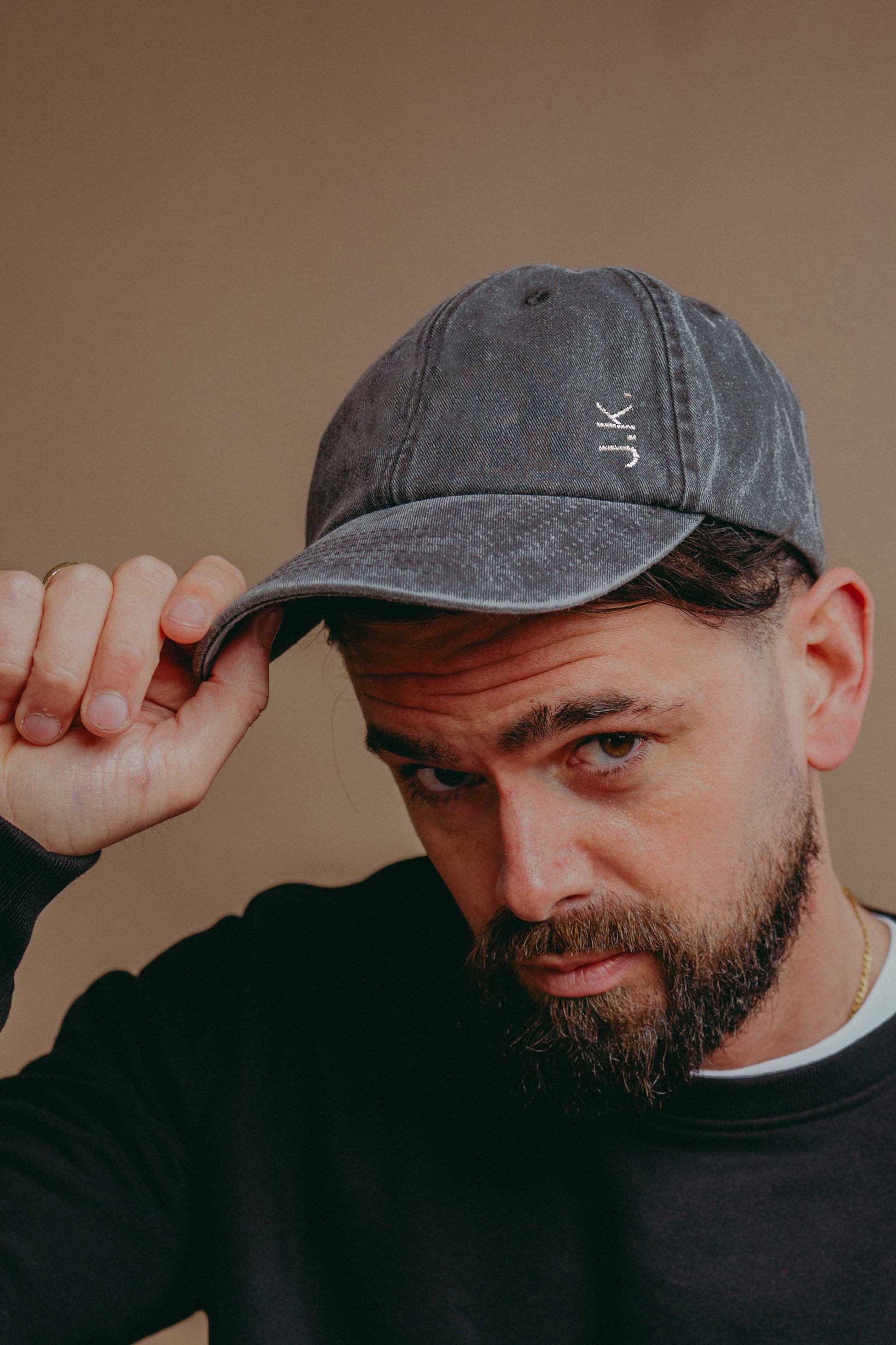 Man wearing a grey cap with 'JK' initials  against a beige background