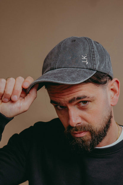 Man wearing a grey cap with 'JK' initials  against a beige background