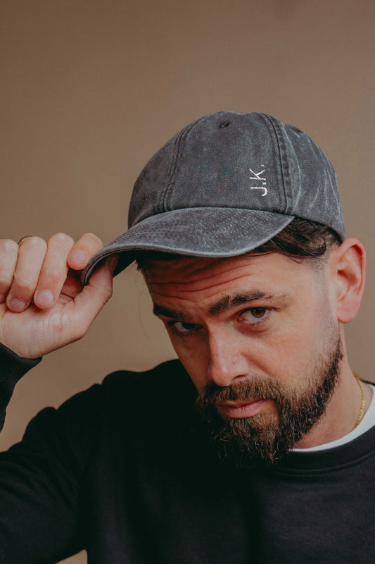 Man wearing a grey cap with 'JK' initials  against a beige background