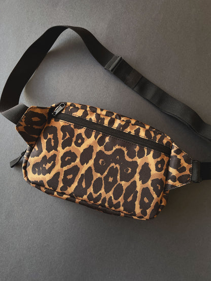 A leopard print bag with a black adjustable strap, shown on a dark grey background.