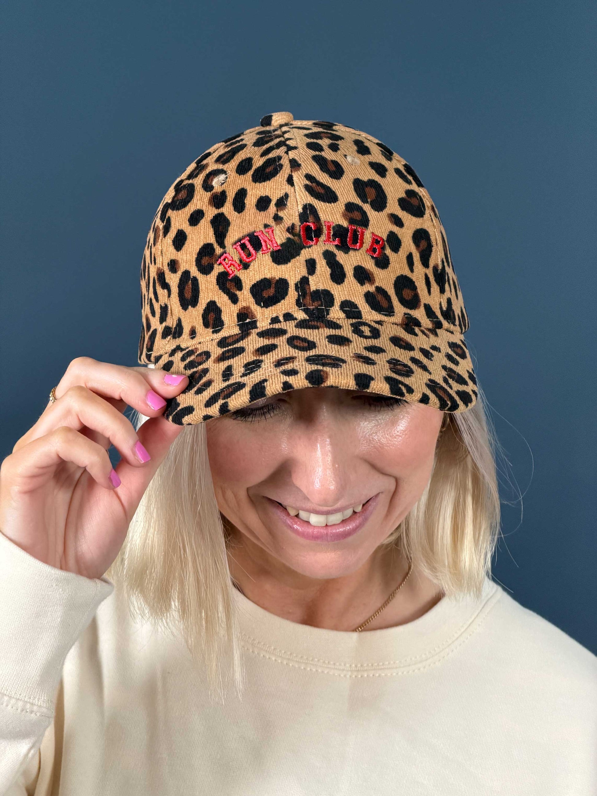 woman wearing leopard print baseball cap embroidered with red curved text run club'
