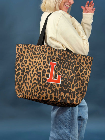woman holding a large leopard print tote bag over her shoulder that is printed with the letter 'L' in red and white text