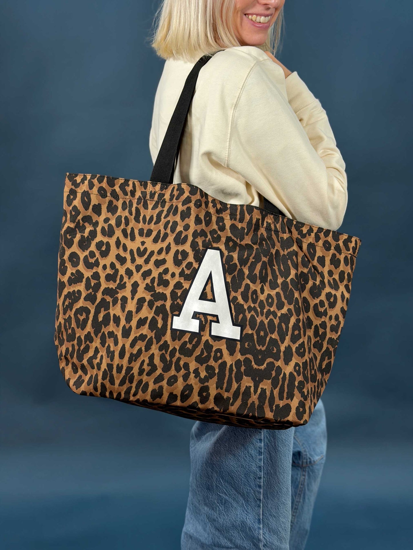 Person holding a leopard print tote bag with a white letter 'A' on a blue background